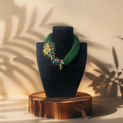 Emerald green seed bead statement necklace with floral design on a black velvet stand against a beige background